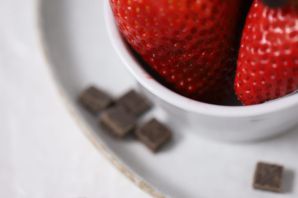 strawberries in a dish with a chunks of dark chocolate next to the dish.